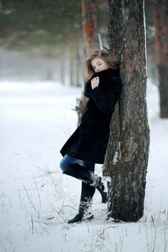 a woman leaning against a tree in the snow