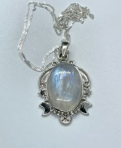 This enchanting pendant showcases a mesmerizing rainbow moonstone with an iridescent glow, set in a beautifully detailed sterling silver setting adorned with celestial stars and a crescent moon. Suspended on a 20" sterling silver chain, this piece captures the magic of the night sky, making it a perfect gift for dreamers and stargazers. This pendant is approximately 1 7/8" long and 1" wide. (not including the bail) Known for its soothing energy and ability to restore balance, the rainbow moonsto Mystical Iridescent Moonstone Necklace, Celestial Moonstone Cabochon Jewelry, Celestial Silver Moonstone Necklace, Silver Celestial Moonstone Necklace, Mystical Silver Moonstone Necklace, Mystical Moonstone Necklace With Sun And Moon Design, Iridescent Moonstone Gemstone Necklaces, Mystical White Moonstone Necklaces, Iridescent Moonstone Gemstone Necklace