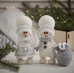 two knitted snowmen holding hands and standing next to each other in front of a christmas tree