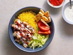 a blue bowl filled with rice, meat and veggies next to two bowls of sauce