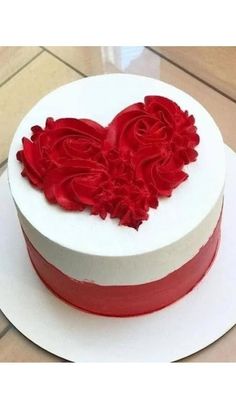 a white cake with red icing and flowers in the shape of a heart on top