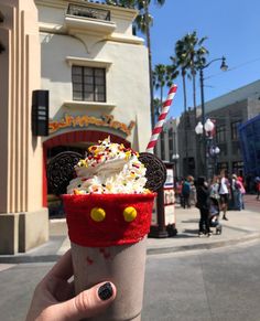 a person holding up a cup with whipped cream and mickey mouse ears on it in front of a building