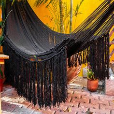 a large black hammock sitting on top of a brick floor next to a potted plant