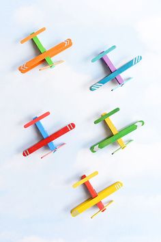 four small toy airplanes are lined up in a row on a white surface with blue sky and clouds behind them