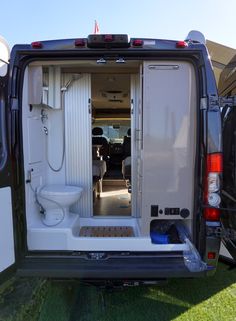 an open van door on the back of a white vehicle with its doors opened and two toilets in it