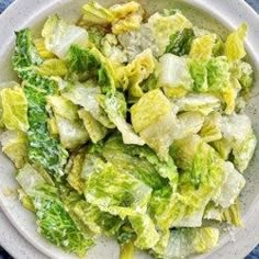 a white bowl filled with lettuce on top of a blue table cloth next to a fork