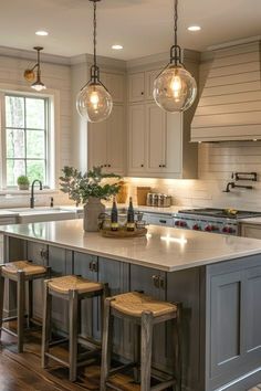 a kitchen island with stools and lights hanging from it's ceiling over the sink