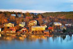 a small town sits on the edge of a body of water in front of a forested hillside