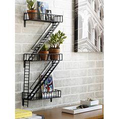 a black metal shelf with plants and books on it next to a white brick wall