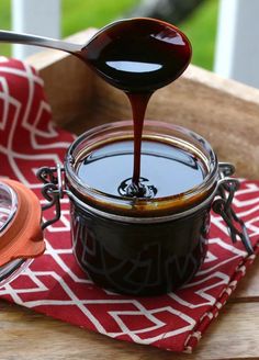 a spoon pouring sauce into a jar on top of a red and white cloth next to an orange napkin