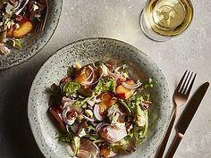 two bowls filled with salad next to silverware and wine glasses on a white table