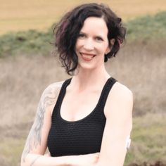 a woman with her arms crossed standing in front of a field and grass, wearing a black tank top