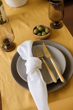 a place setting with silverware, olives and napkin on a tablecloth draped by a gold cloth