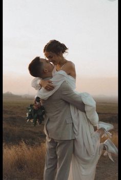 a bride and groom embracing each other in the middle of an open field at sunset