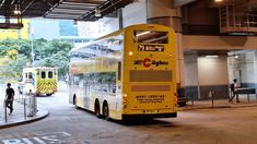 a yellow bus parked in front of a tall building with people walking around it and two men standing on the sidewalk