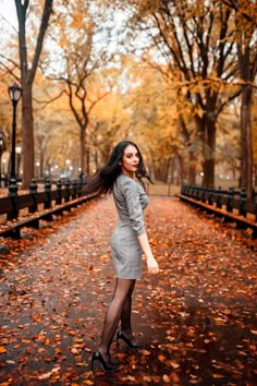 a woman is standing in the middle of an autumn park