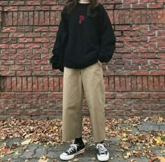 a woman standing in front of a brick wall wearing black sweatshirt and khaki pants