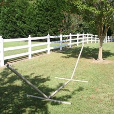 a white fenced in area with a tree and some poles on the grass next to it