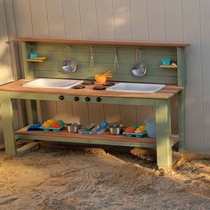 an outdoor play kitchen with two sinks and pots on the top shelf, next to a wall