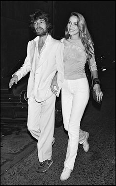 a man and woman walking down the street in white outfits with one holding his hand