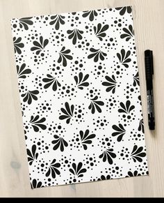 a black and white flower pattern on a notebook with a pen next to it,