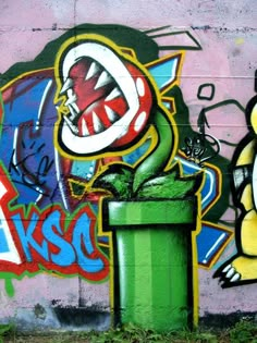 graffiti on the side of a building with a green trash can and a yellow cat