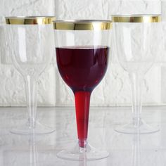 three wine glasses sitting on top of a counter next to each other with red liquid in them