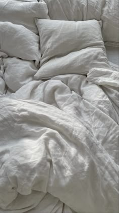 an unmade bed with white sheets and pillows