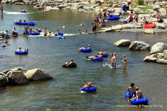 many people are in the water with rafts and swimming on large rocks while others float down them