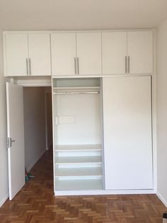 an empty room with white cupboards and wood parquet flooring in the middle