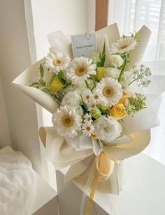 a bouquet of white and yellow flowers in a gift box on a window sill