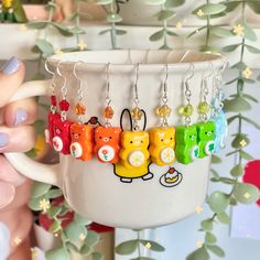 a person holding a cup with bear charms hanging from it's sides, in front of a plant