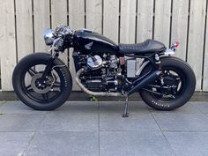 a black motorcycle parked next to a wooden fence on top of a cement floored area