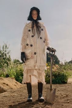 a woman in a white dress and hat holding a shovel