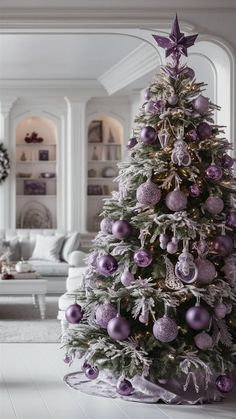 a decorated christmas tree in a living room with white furniture and purple ornaments on it