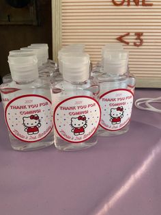 four bottles with hello kitty labels on them sitting on a purple tablecloth next to a sign