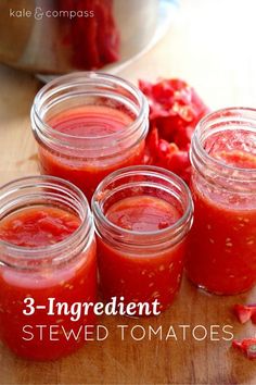 four jars filled with red sauce sitting on top of a wooden table