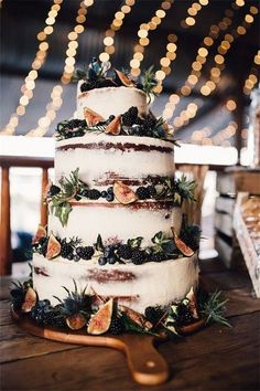 a three tiered cake with berries and greenery sits on top of a wooden table