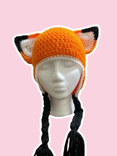 an orange and white knitted hat with black tassels on top of a mannequin's head