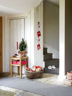 a christmas tree in a basket on the floor next to a table with presents under it