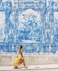 a woman in a yellow dress walking past a blue and white wall