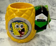 a yellow mug with an image of a cartoon character on it and a tag hanging from the handle