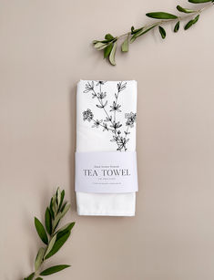 two tea towels on top of each other next to some green leaves and branches in the background