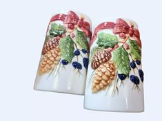 two white vases with pine cones and berries painted on them