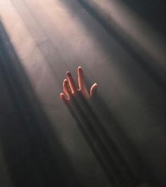 a person's hands reaching up into the air with sunlight streaming through them on a dark background