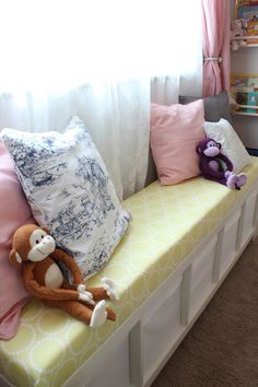 a stuffed monkey sitting on top of a yellow bench next to pillows and a window