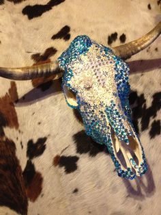 a cow skull with blue and white sequins on it's head sitting on a cow skin