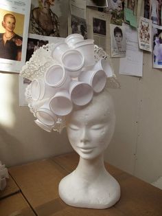 a white mannequin head with lots of cups in it's hair on top of a table