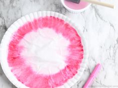 a paper plate with pink and white dye on it, next to a paintbrush