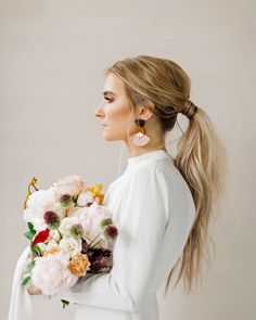 a woman with long hair holding a bouquet of flowers in her hand and wearing earrings